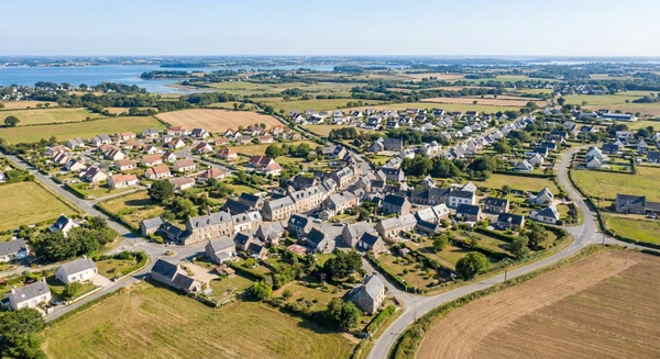 Vue aérienne ou paysagère de Plougoumelen montrant son tissu urbain, ses quartiers résidentiels, ses routes d'accès et ses alentours ruraux caractéristiques de la Bretagne sud, photographiée en journée avec une bonne luminosité naturelle. L'image doit transmettre l'accessibilité et la proximité de Plougoumelen comme base d'intervention de l'entreprise. Photographie réaliste de haute qualité professionnelle sans texte, logo ou filigrane visible.
